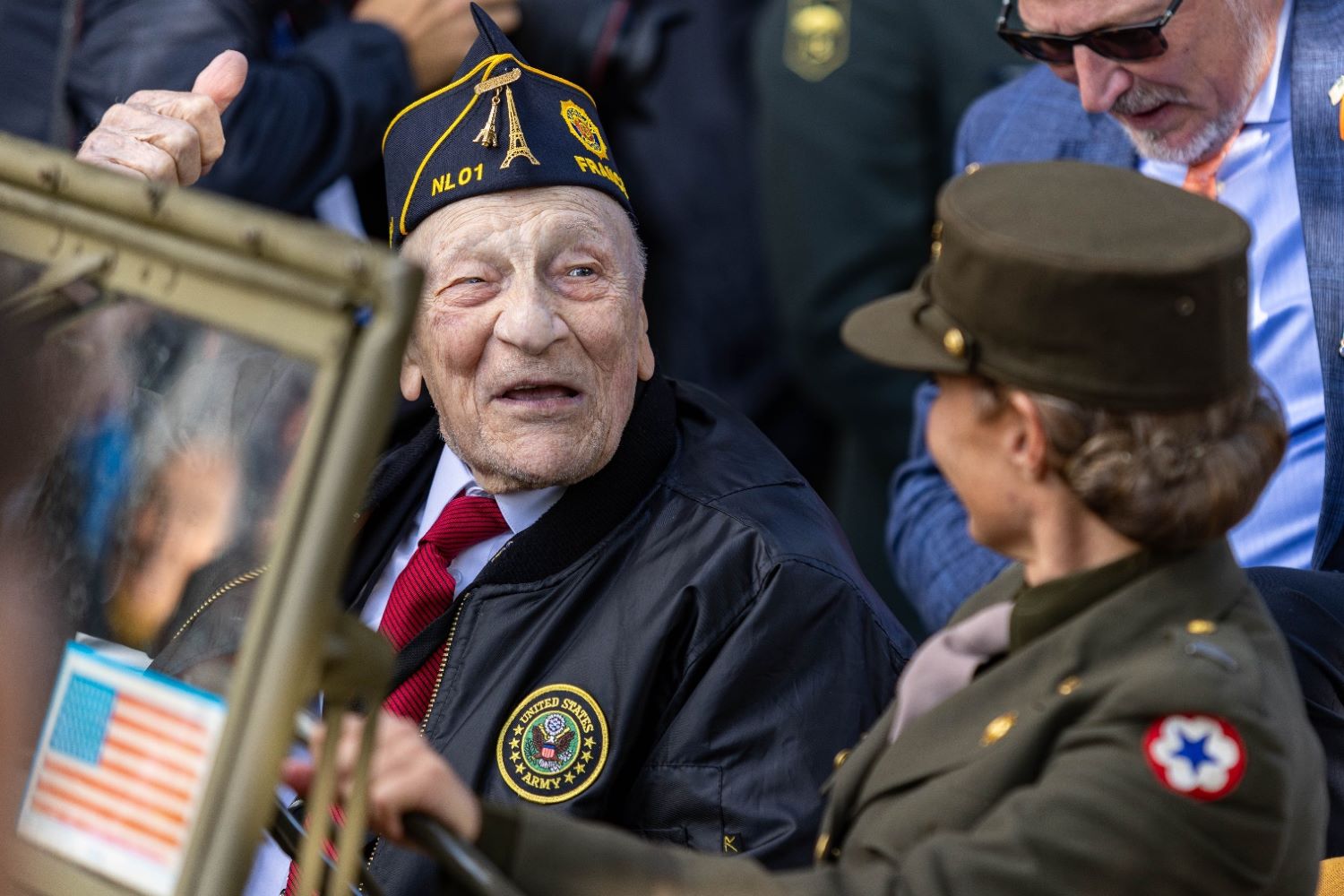 a World War II veteran gave a thumbs-up while riding in a vintage U.S. Army Jeep during the opening ceremony