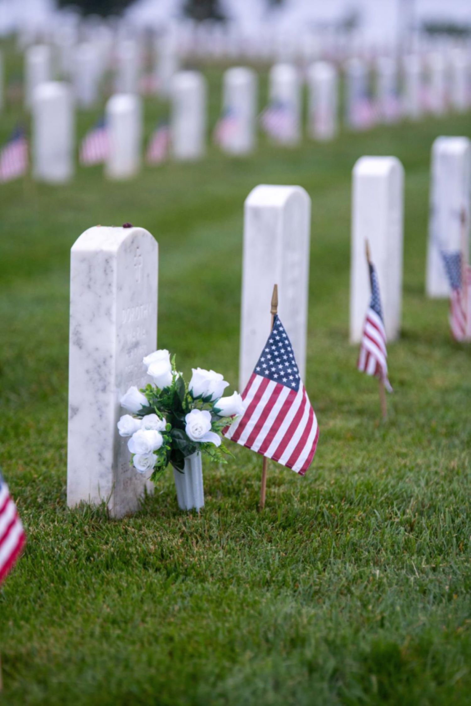 a small bouquet of white roses and an American flag at a gravestone